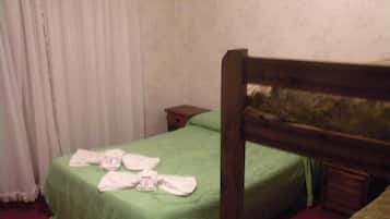 Una cama individual con una colcha verde y un cabecero de madera. Hay toallas sobre la cama.