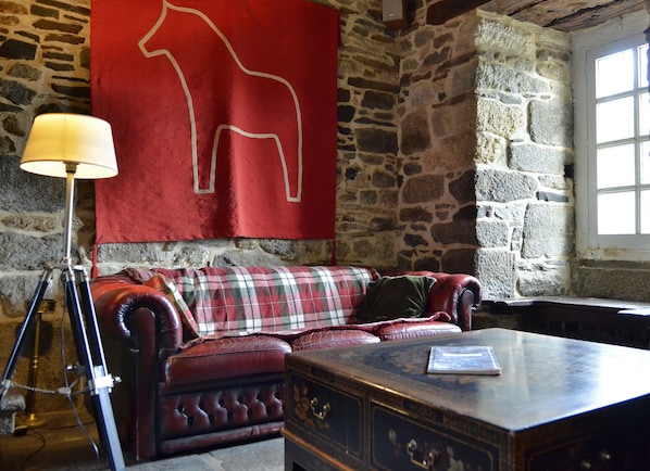 Een gezellige kamer met een stenen muur, een rode bank met een geruite plaid, een lamp en een houten tafel.