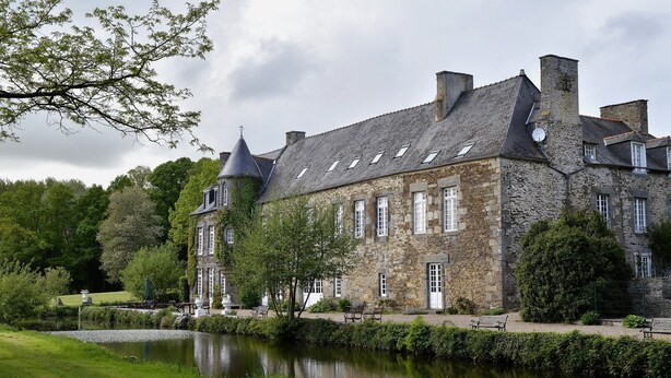 Een stenen gebouw met een vijver ervoor, met een gazon en banken.