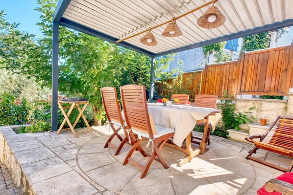 Eine Terrasse im Freien mit Tisch und Stühlen, umgeben von Pflanzen und einem Holzzaun.