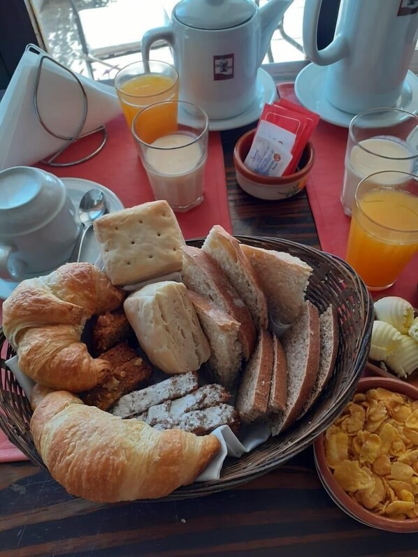 A breakfast table with croissants, bread, biscuits, and cereal. There are also cups of coffee and orange juice. - Posada la Villa (Villa Carlos Paz)