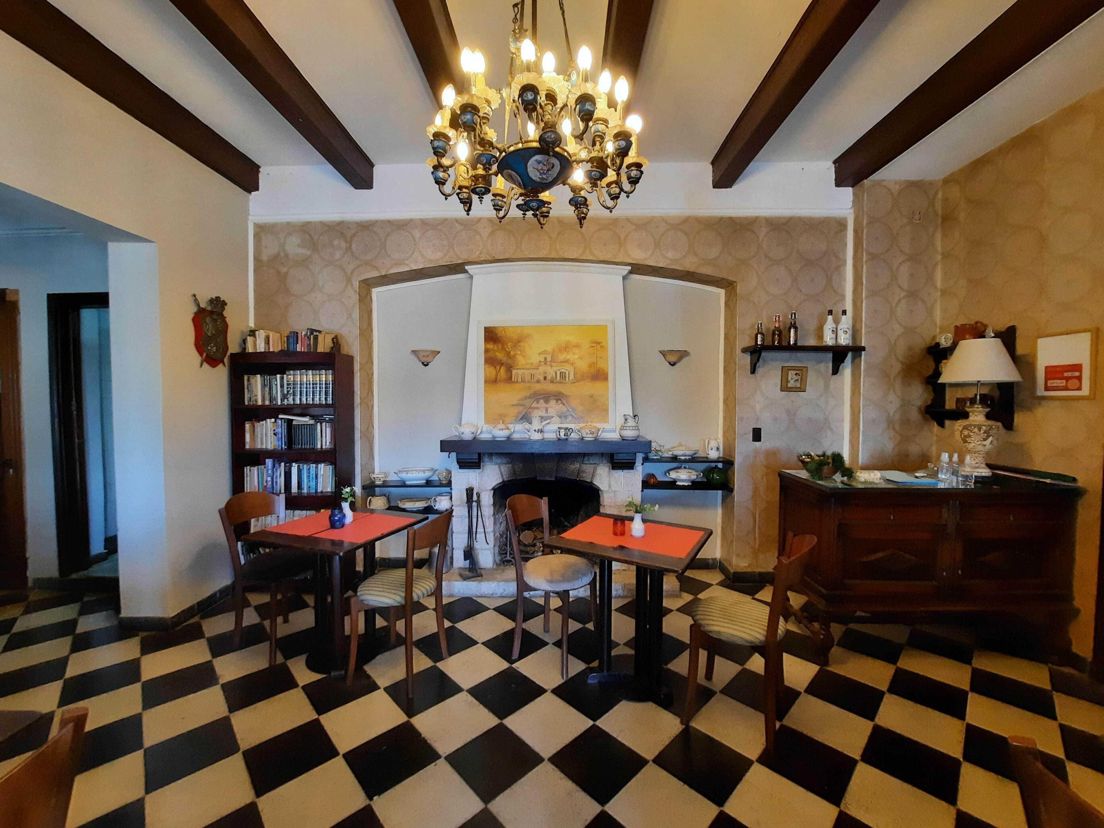 A dining area with a checkered floor, a chandelier, a fireplace, and a bookshelf.