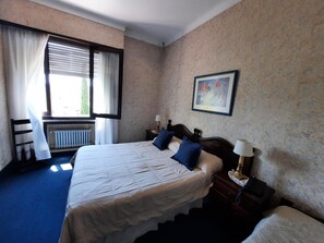 A bedroom with a large bed, two bedside tables with lamps, a window with curtains, a radiator, and a framed picture on the wall. - Posada la Villa (Villa Carlos Paz)