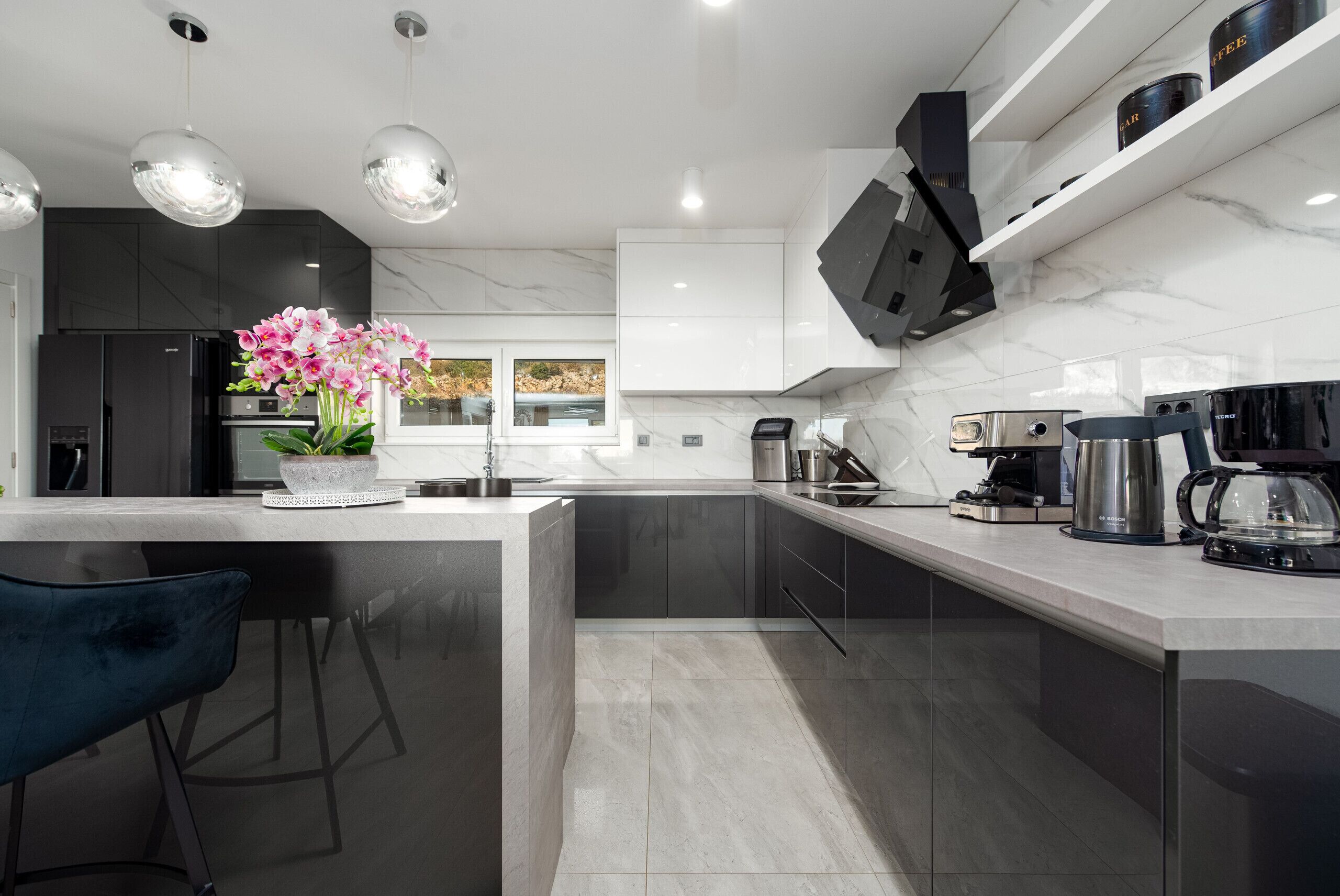 A modern kitchen with a marble countertop, stainless steel appliances, and a potted orchid centerpiece.