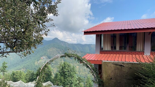 Un edifici amb un teulat vermell, vista de muntanyes verdes i cel serè.