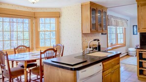 A kitchen with wooden cabinets, a dishwasher, a sink, and a dining table with chairs. - 141 Harlow Road (Sandwich)