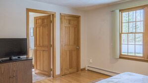 A room with wooden doors, a television on a cabinet, and a window with a view of trees. - 141 Harlow Road (Sandwich)