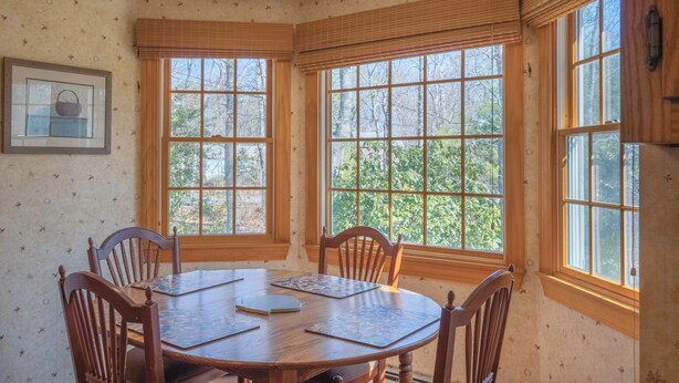 A dining room with a wooden table and chairs, large windows with blinds, and a framed picture on the wall. - 141 Harlow Road (Sandwich)