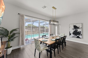A dining area with a pool view, a modern chandelier, and a large abstract painting.