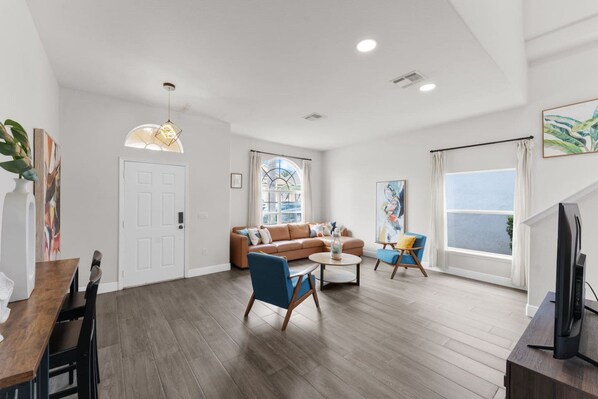 A modern living room with a brown sofa, blue armchairs, a wooden coffee table, and a TV. - 451 Davenport 5BR House with Heated Pool and Grill (Davenport)