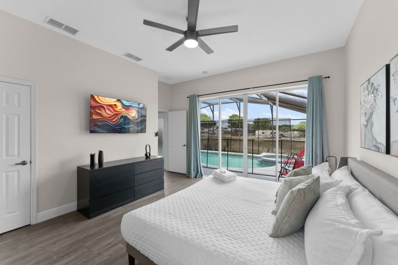 Une chambre avec un grand lit, une commode, un ventilateur de plafond et une vue sur une piscine.