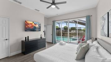A bedroom with a large bed, a dresser, a ceiling fan, and a view of a swimming pool.