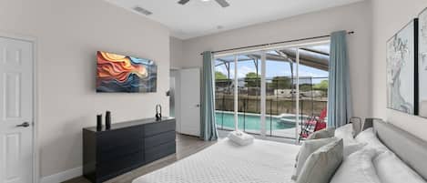A bedroom with a large bed, a dresser, a ceiling fan, and a view of a swimming pool.