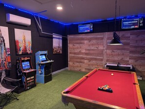 Ein Raum mit Poolbillardtisch, Spielautomaten und Wandbildern.