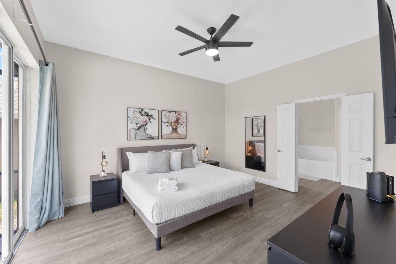 A modern bedroom with a large bed, bedside tables, a ceiling fan, and artwork on the walls.