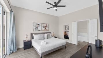 A modern bedroom with a large bed, bedside tables, a ceiling fan, and artwork on the walls.