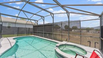 A covered swimming pool with a view of a fenced area and a building in the background.