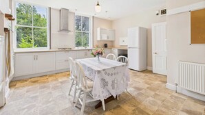 A modern kitchen with white cabinetry, a dining table with a floral tablecloth, and a view of greenery through large windows. - Host Stay Thornecroft (Knaresborough)