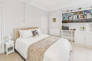 A bedroom with a large bed, a bedside table with a lamp, a bookshelf filled with books, and a radiator. - Host Stay Thornecroft (Knaresborough)
