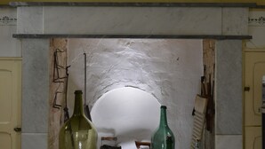 A room with a white fireplace, two green bottles, and a wooden chair.