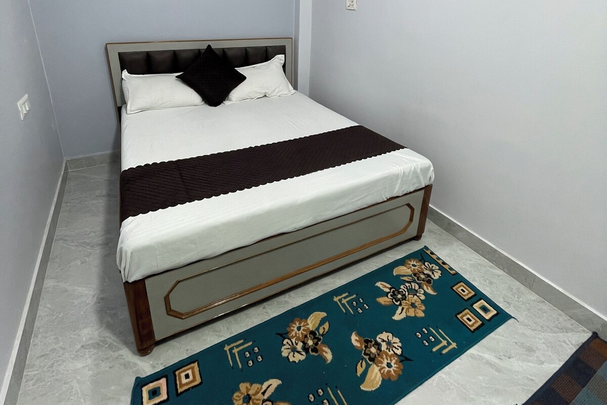 A bedroom with a bed, a wall-mounted fan, and a patterned rug.