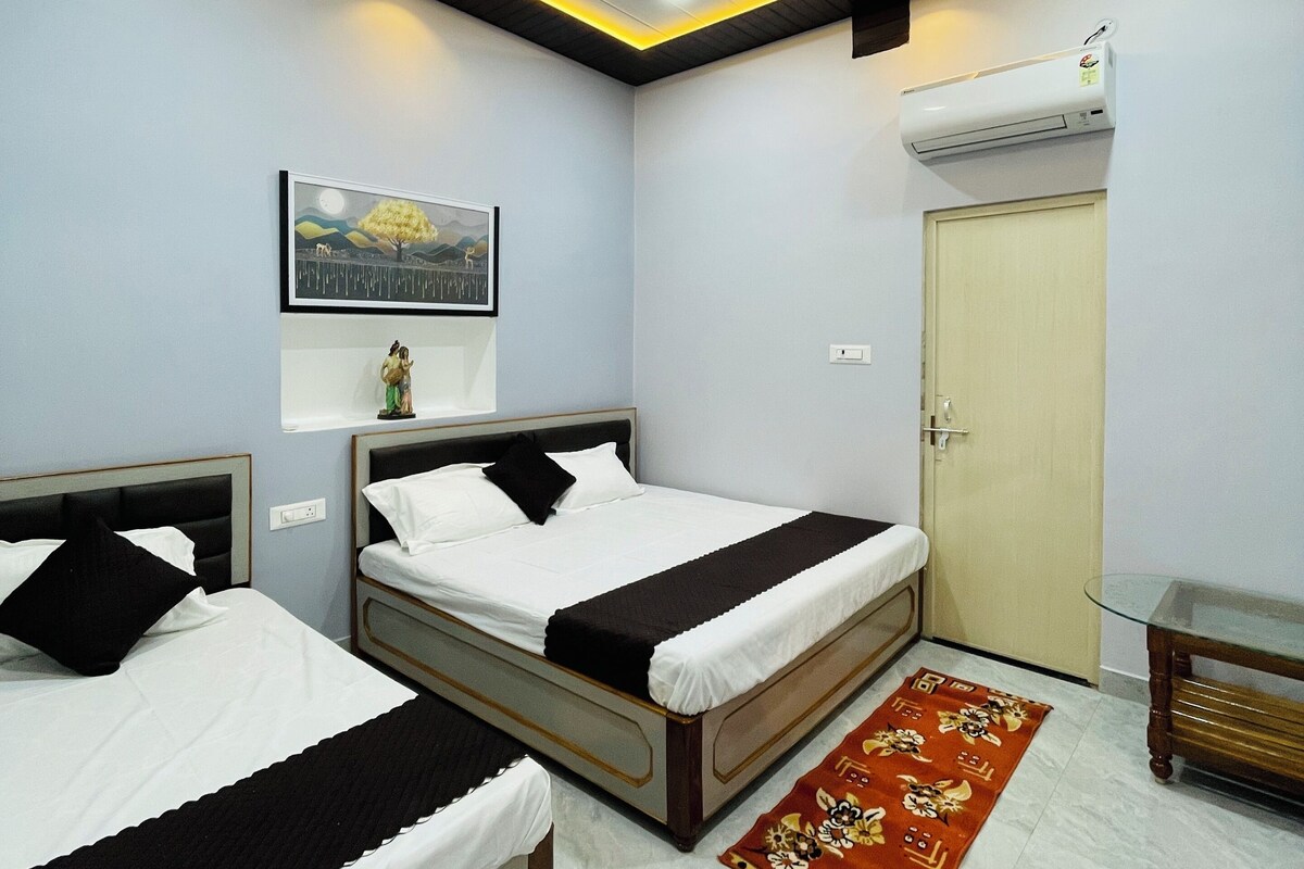 A hotel room with two beds, a ceiling fan, an air conditioning unit, a framed picture on the wall, and a small table with a glass top.