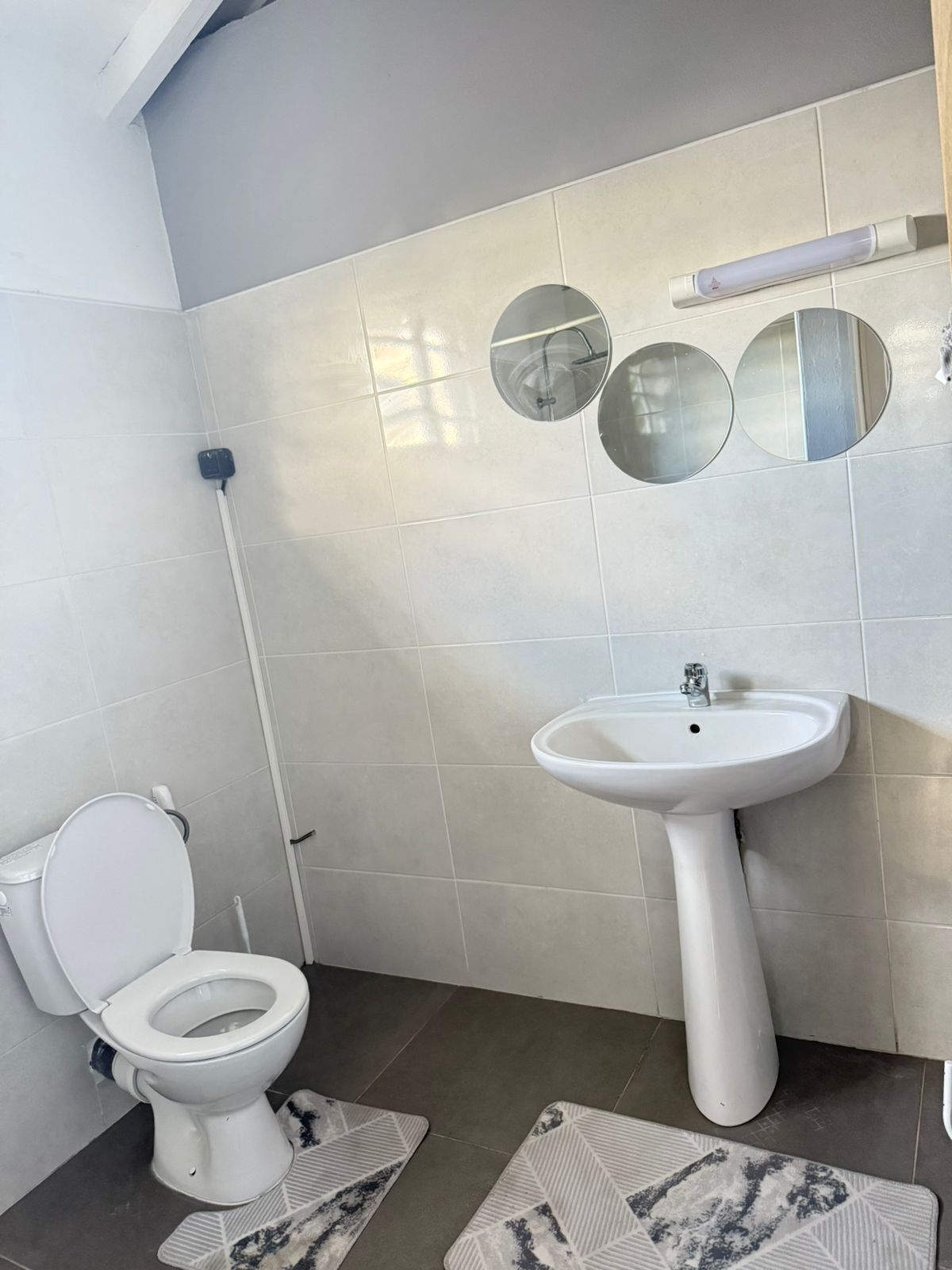A bathroom with a toilet, sink, and three round mirrors on the wall.