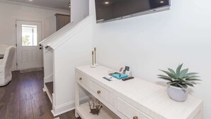 A modern interior with a staircase, a white console table with decorative items, and a mounted TV. - Grover at Meadowcrest by Apex Short Term Stays (Oxford)