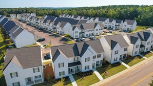 A row of modern, single-story townhouses with attached garages, arranged in a linear fashion along a street. - Grover at Meadowcrest by Apex Short Term Stays (Oxford)