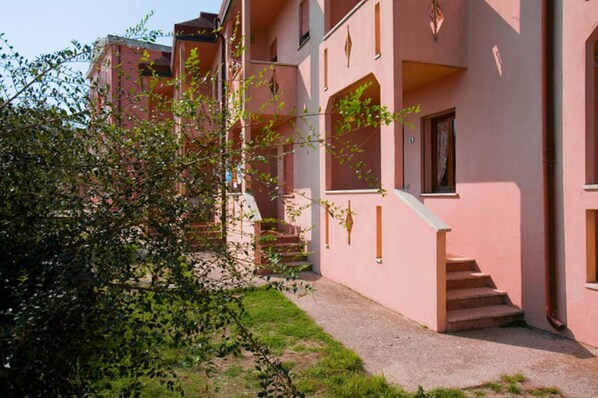 A pink building with a staircase leading to a door, surrounded by greenery.