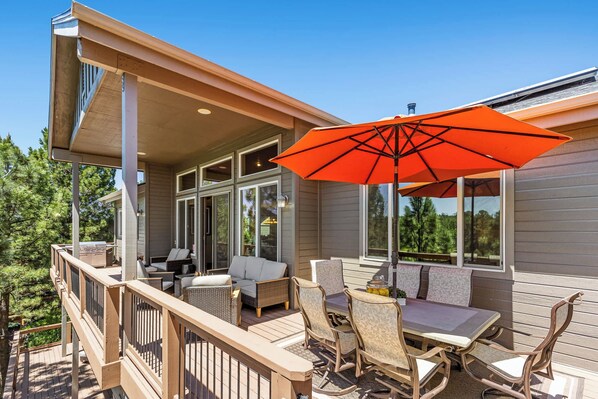 Una terraza techada con mobiliario exterior, incluyendo una mesa y sillas, y un gran paraguas naranja.