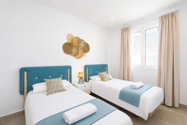 A hotel room with two beds, a nightstand with a lamp, a decorative wall hanging, and a window with curtains. - Villa Maria 7 - Three Bedroom Villa, Sleeps 6 (Puerto Calero)