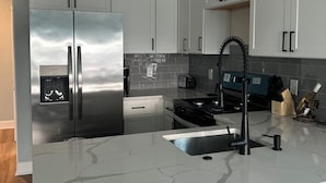 A modern kitchen with white cabinets, a stainless steel refrigerator, a black faucet, and a marble countertop.