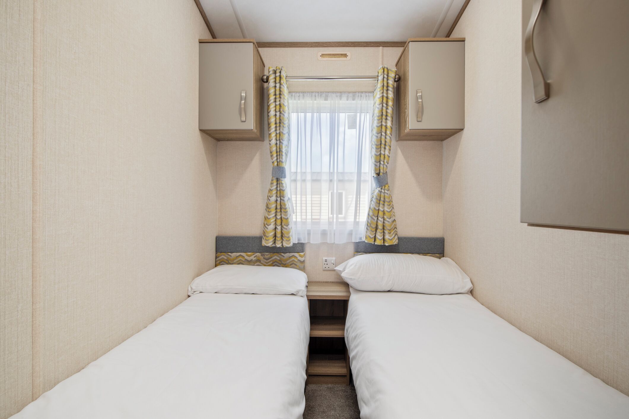 A compact bedroom with two single beds, a small table, and a window with curtains.