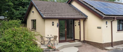 A house with a sloped roof, solar panels, a patio with a table and chairs, and a stone wall.