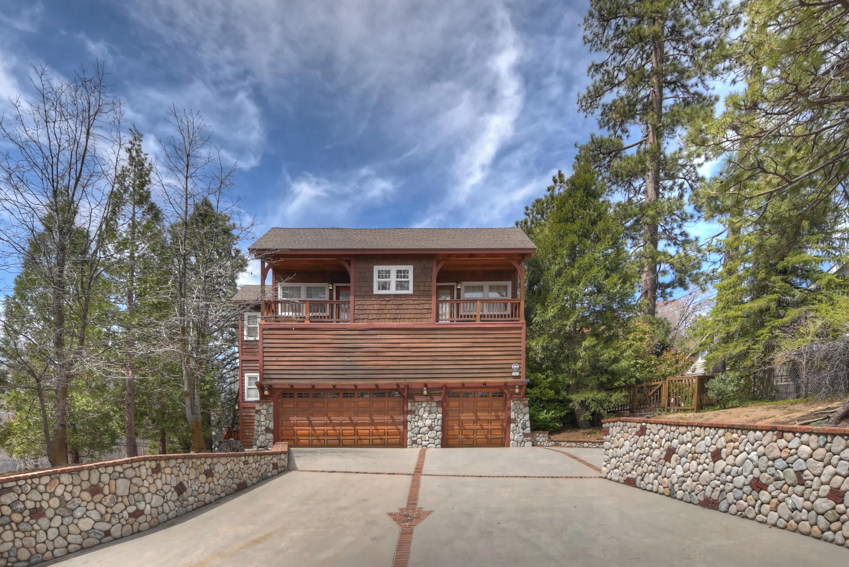 A two-story log cabin with a stone retaining wall, a garage with wooden doors, and a clear sky.