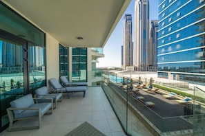 A balcony with lounge chairs, a pool, and high-rise buildings in the background.
