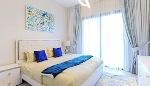 Une chambre à coucher avec un grand lit, une table de chevet, une lampe, un tableau et une vue sur l’extérieur.