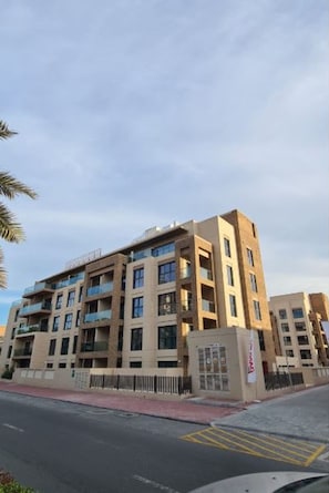 Un immeuble résidentiel à plusieurs étages, doté de balcons, d’une entrée sécurisée et surplombant un ciel dégagé.