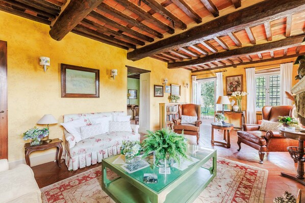 A cozy living room with a wooden ceiling, a sofa, a coffee table, and a fireplace. - Iconic Romantic Farmhouse with Pool in Lucca (Lucca)