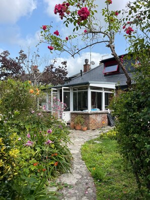 A house with a conservatory, surrounded by a garden with various plants and flowers.