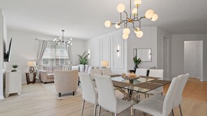 A modern dining area with a glass-top table, white chairs, and a chandelier. - 3BR Condo w/ Game Room, Themed Rooms, Top Location (Orlando)