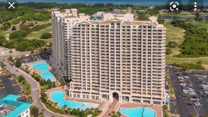 A high-rise hotel with multiple balconies, a central courtyard, and two swimming pools.
