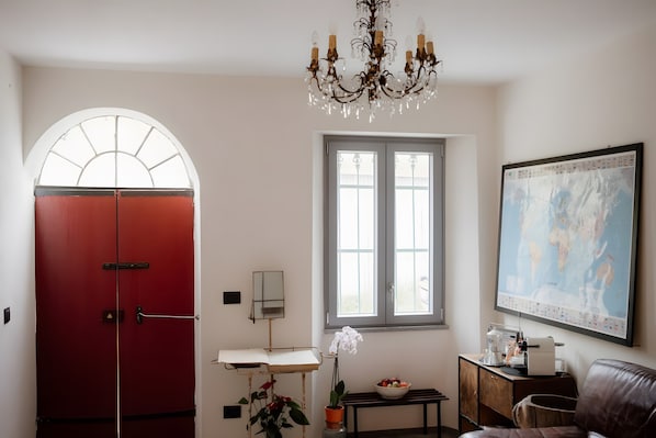 A room with a red door, a chandelier, a window, a map on the wall, a bench, and a coffee machine.