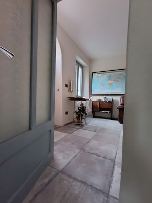 A hallway with a tiled floor, a map on the wall, a potted plant, and a wooden cabinet.