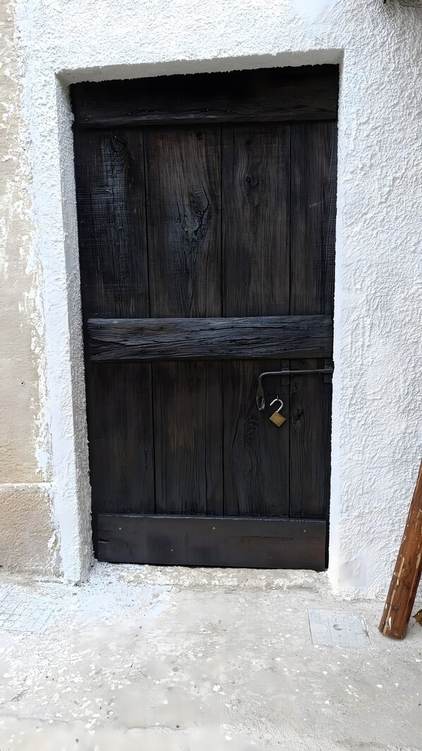 Una porta de fusta fosca amb un cadenat metàl·lic, situada a una paret blanca amb textura i un sòl de formigó.