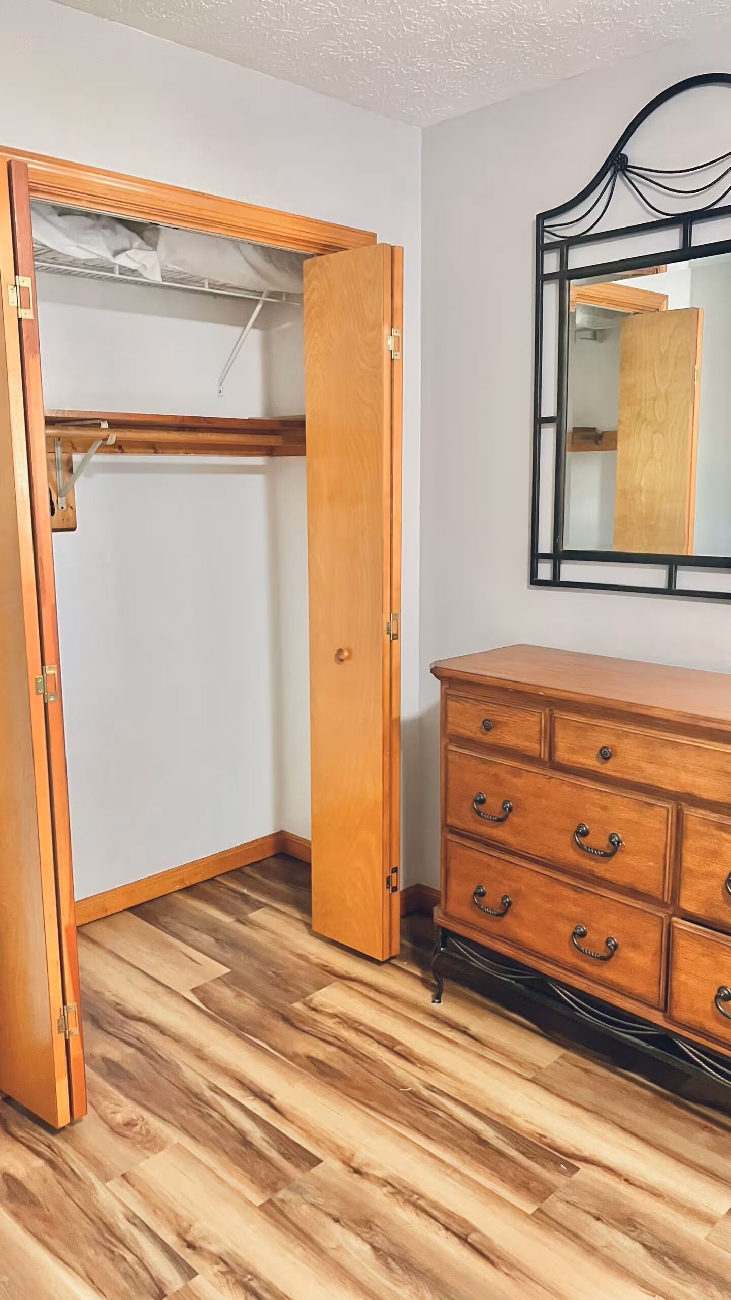 A room with a wooden wardrobe, a dresser with drawers, and a mirror on the wall.