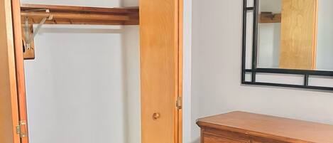 A room with a wooden wardrobe, a dresser with drawers, and a mirror on the wall.