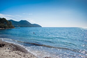 A beach with clear water, a sandy shore, and a mountain in the background. - Holiday Home 'Es Port Nou - Casa En La Playa' with Sea View, Private Terrace and Wi-Fi (Son Servera)