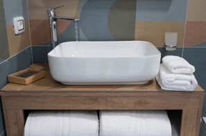Une salle de bain avec un lavabo rectangulaire blanc, un meuble-lavabo en bois et un porte-serviettes avec des serviettes pliées.